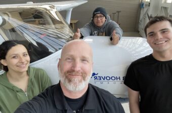 A photo of an educator and three of his students taking a photograph in front of an airplane.