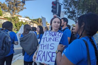 A group of people standing together in blue shirts with one holding a sign that reads "Project Tune This Raise."